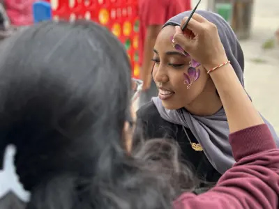 A face painter is applying a painted design to a young womans face