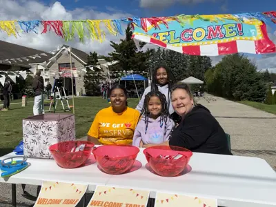 girls sitting behind a table with buckets of treats in front of them at a festival