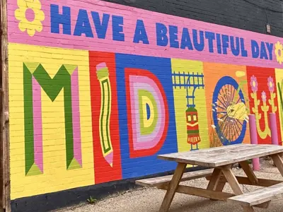 a colourful mural that says "Have a Beautiful Day Midtown" with a wooden picnic table in front of it