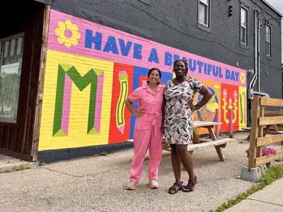 2 women posing in front of a brightly coloured mural on the wall of a building
