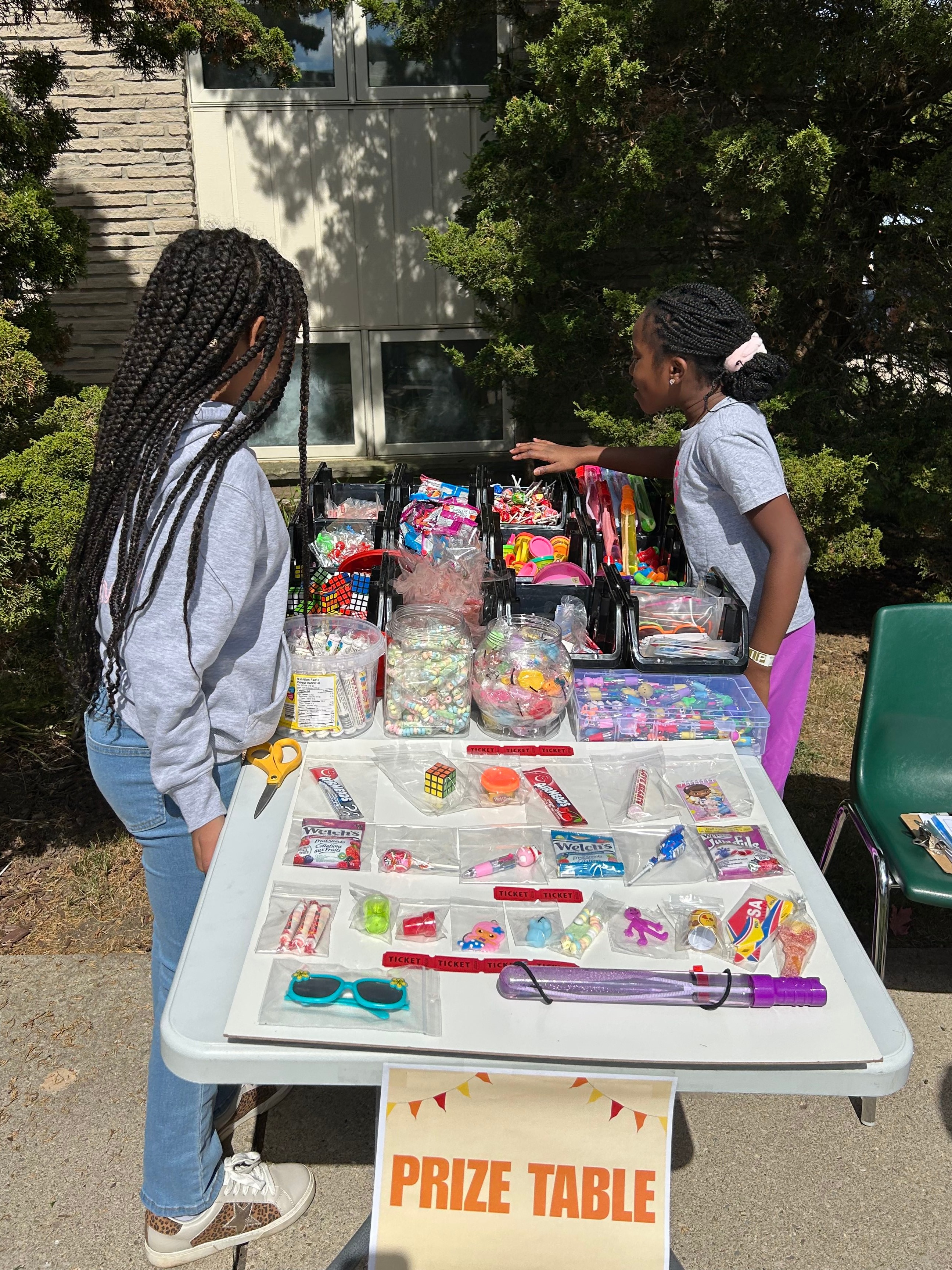 girls standing beside table displaying handmade items for sale