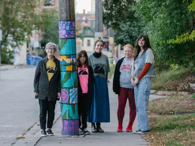 women posing for photos beside a telephone pole with knitted squares on it